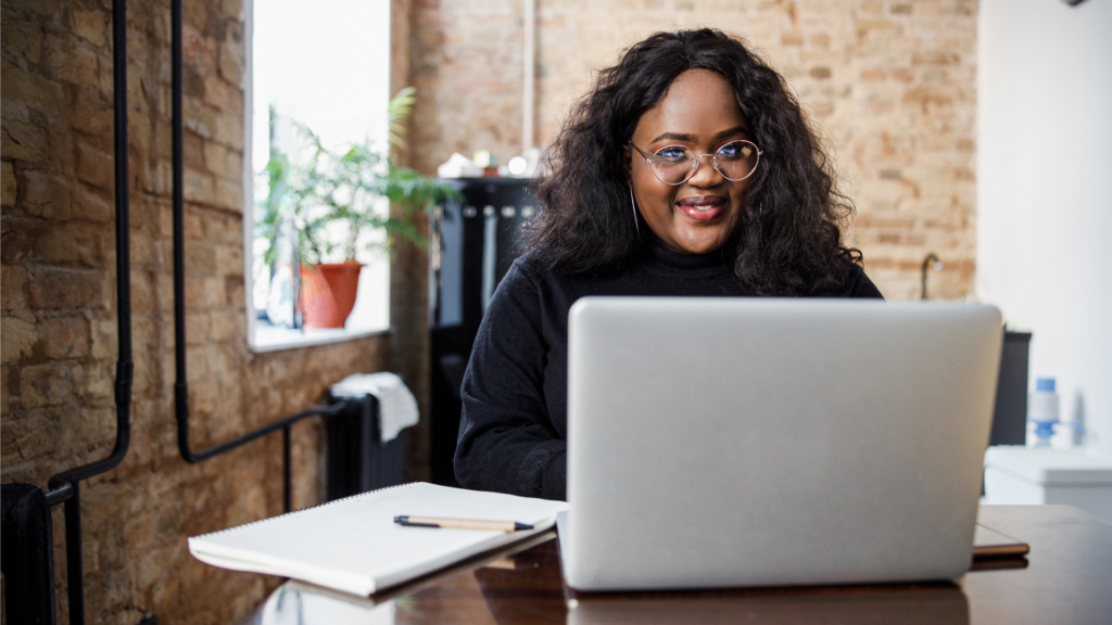 Una ragazza con occhiali rotondi siede alla scrivania e sorride mentre scrive al computer.
