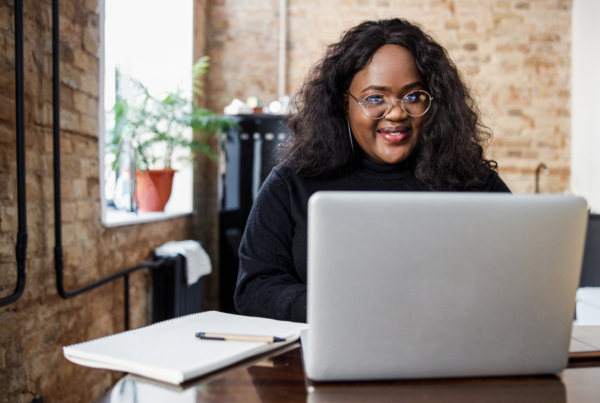Una ragazza con occhiali rotondi siede alla scrivania e sorride mentre scrive al computer.